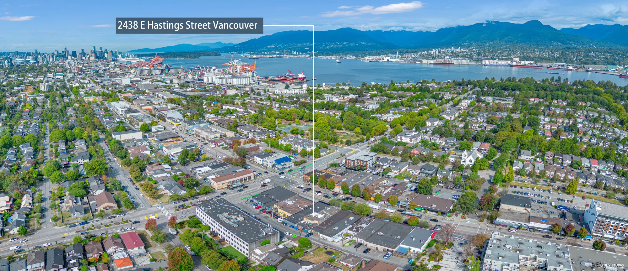 Wide aerial panorama looking north over the Hastings strip to the port, Burrard Inlet and the North Shore mountains, with 2438 E Hastings Street marked
