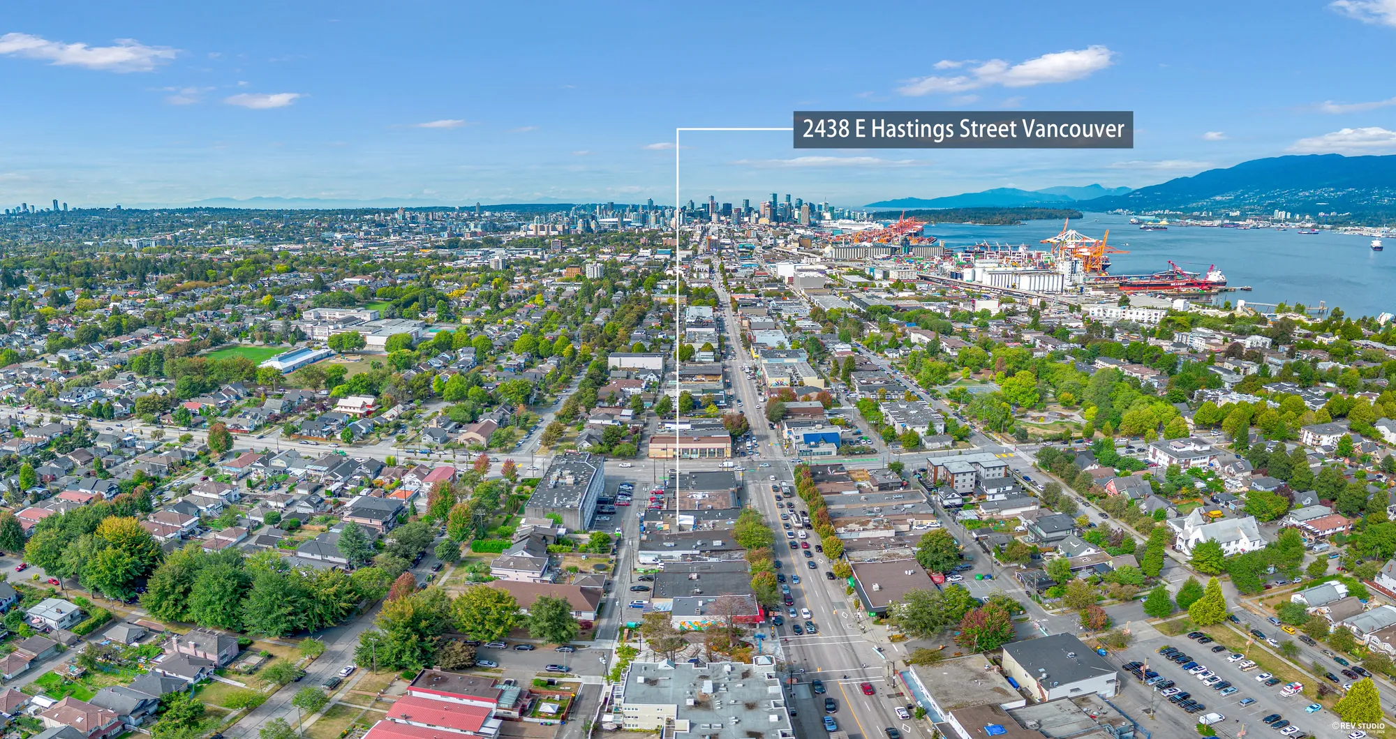 Wide aerial panorama looking west along East Hastings Street toward the downtown Vancouver skyline, with 2438 E Hastings Street marked