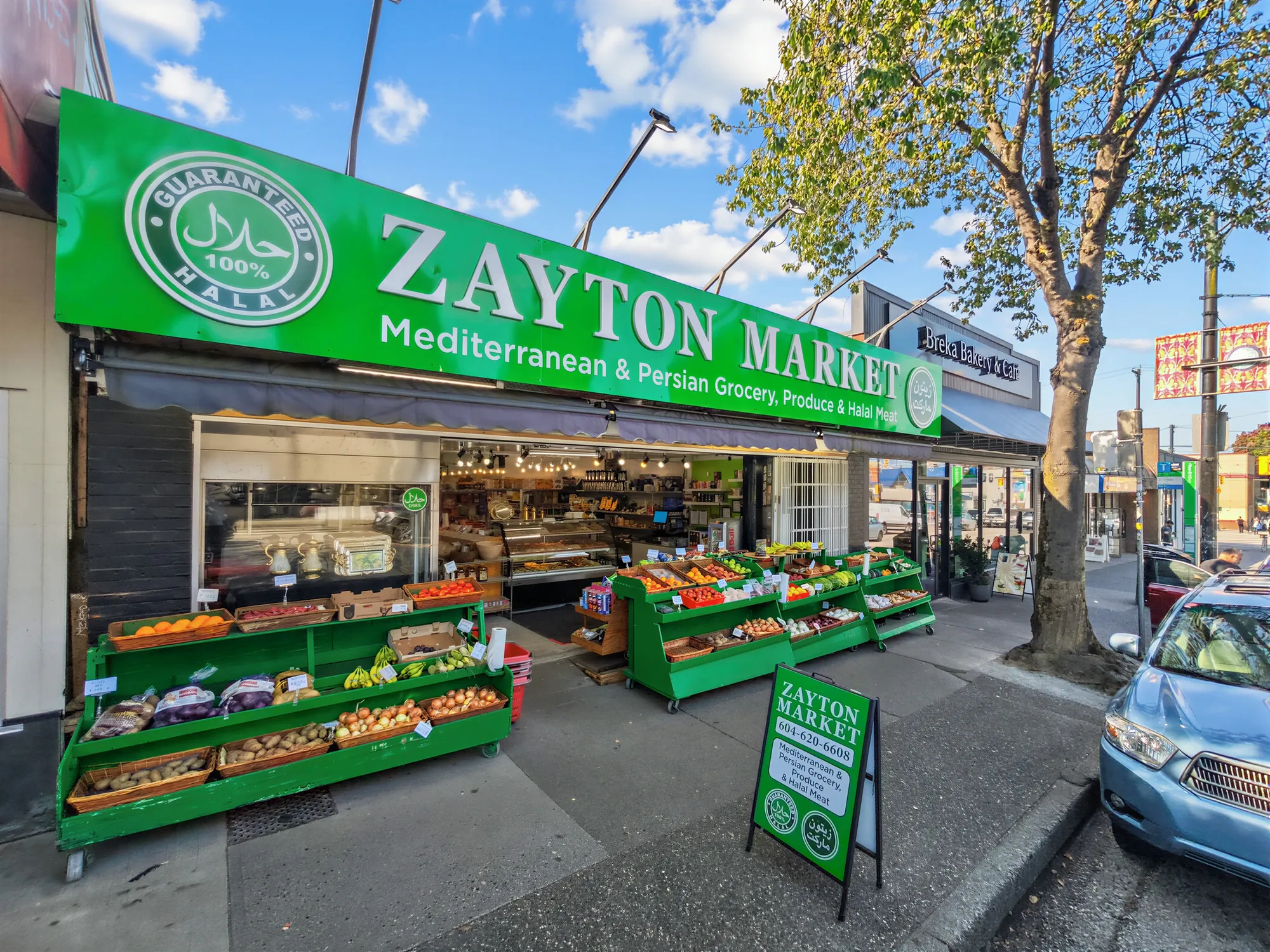Zayton Market storefront straight on, produce tables under the green sign